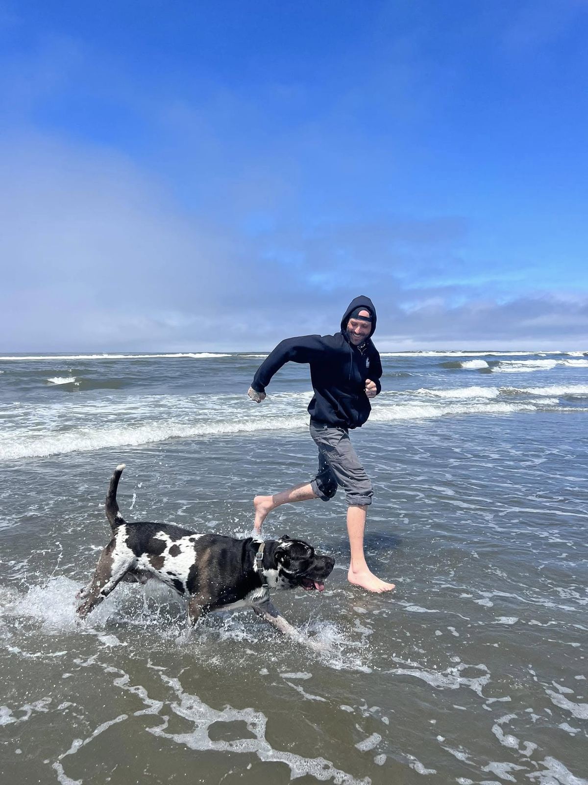 Scoop running barefoot through the surf with Dude, his black and white Great Dane, splashing beside him