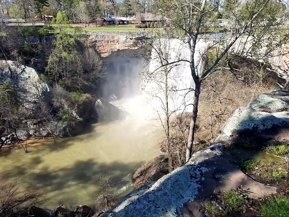 A waterfall pouring into a muddy spring river below rocky cliffs and bare trees